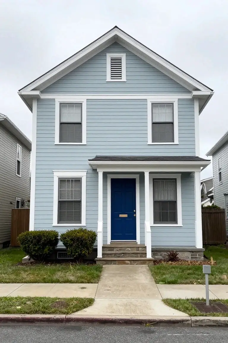 Light blue two-story house with white trim, blue front door, and simple landscaping
