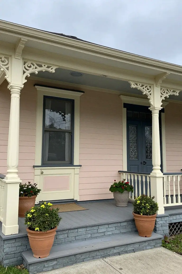 Pale blush pink house exterior with white trim, navy blue door and window frames, and potted plants on the porch