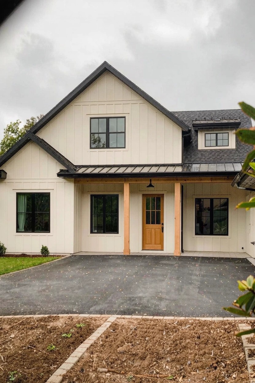 Modern farmhouse house exterior with warm greige siding, black window trim, dark gray roof, and yellow wood front door under a cloudy sky