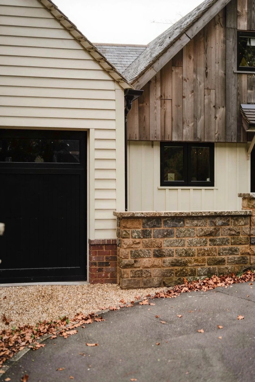 Farmhouse exterior featuring warm creamy white clapboard siding paired with wood panels, black garage door, and brick accents