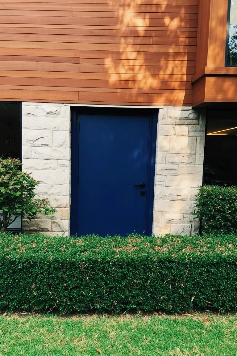 Deep navy blue front door against warm wood siding and stone walls with green hedges