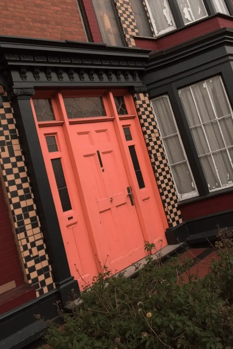 Bright orange-red front door on a brick house with black trim and checkered tile accents