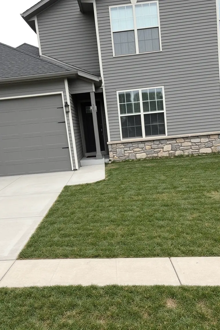 Two-story house with cool medium gray siding, white trim, stone base, and attached garage on a grassy lot