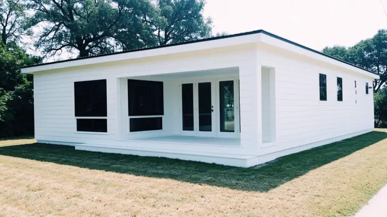 Small modern home with crisp white clapboard siding, black-framed windows and door, on a grassy yard with trees