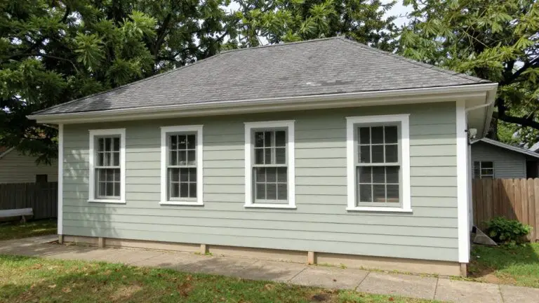 Small seafoam green house with white trim, gable vent, and triple window under trees