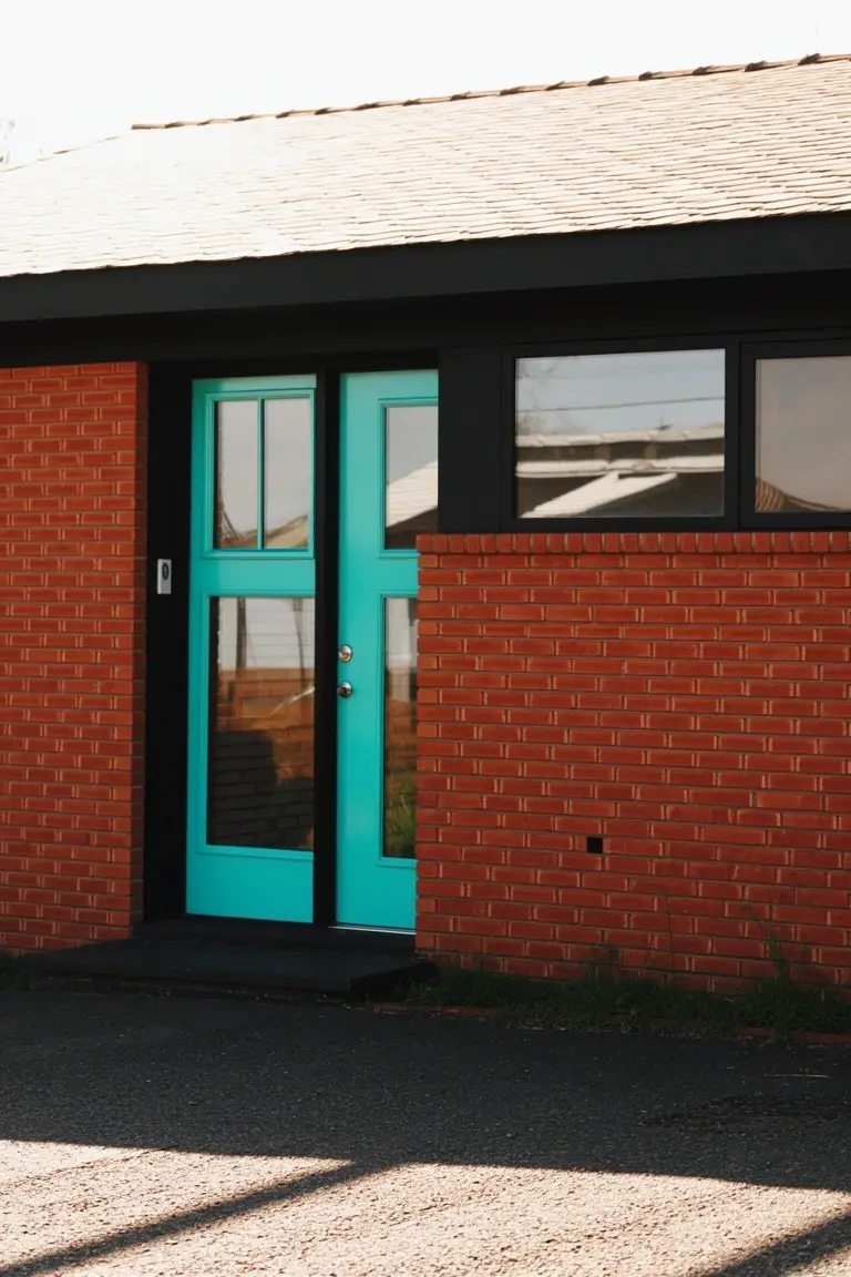 Vibrant teal double door on brick house exterior with black trim framing