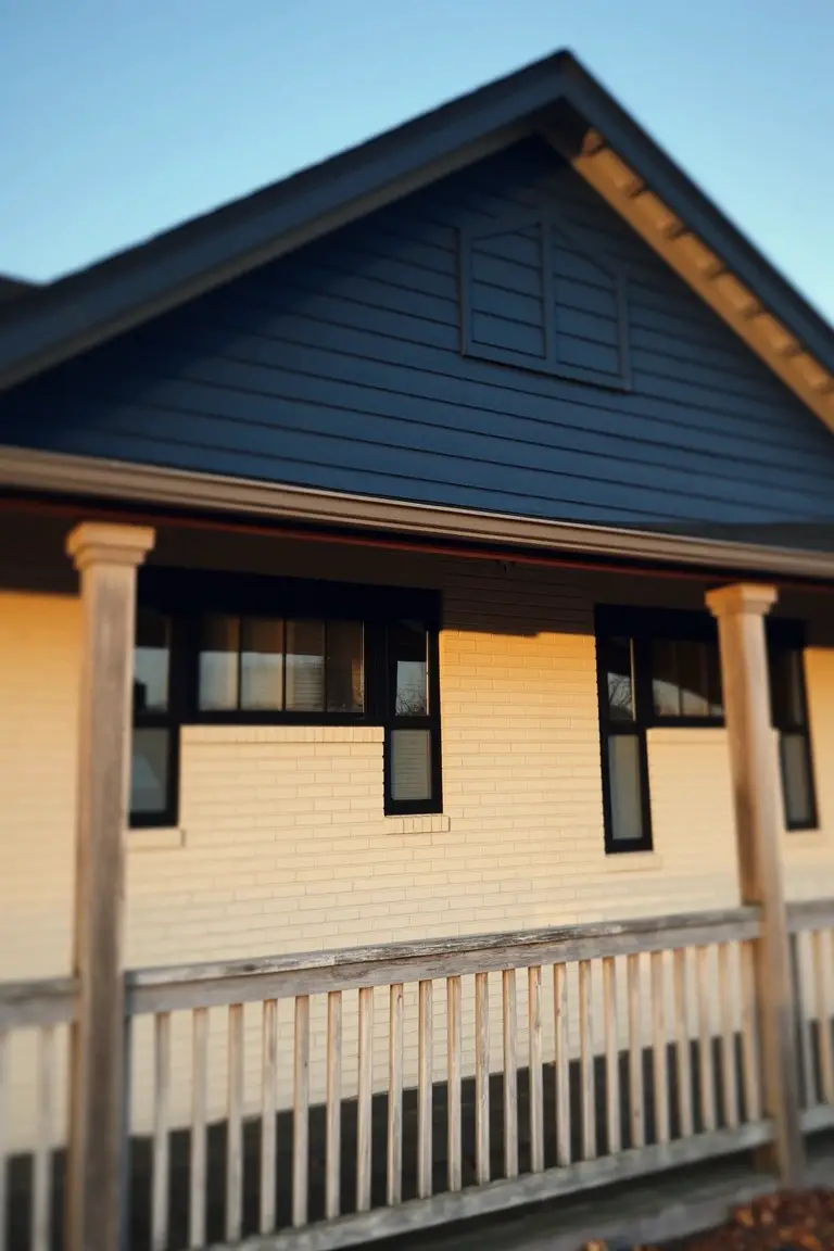 Beige brick house with deep navy upper siding, white-trimmed windows, and wooden porch columns