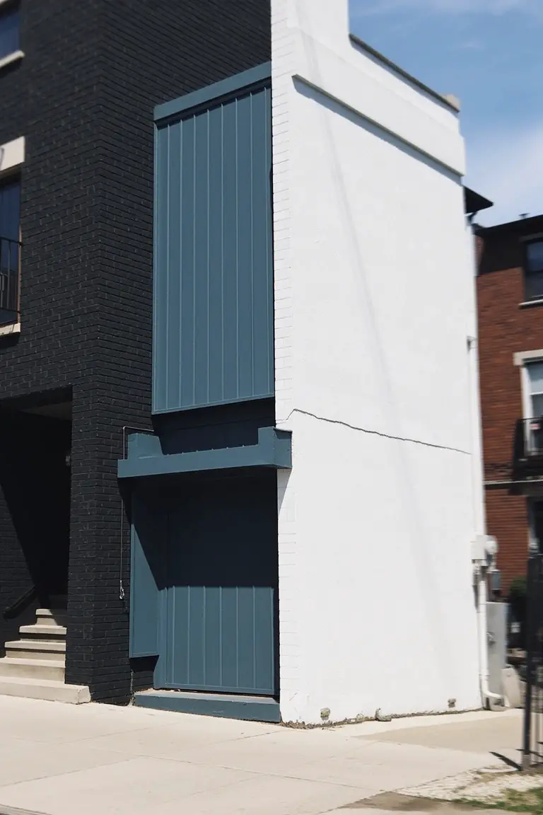 Modern brick home exterior featuring muted teal siding panels and garage door between black and white brick walls