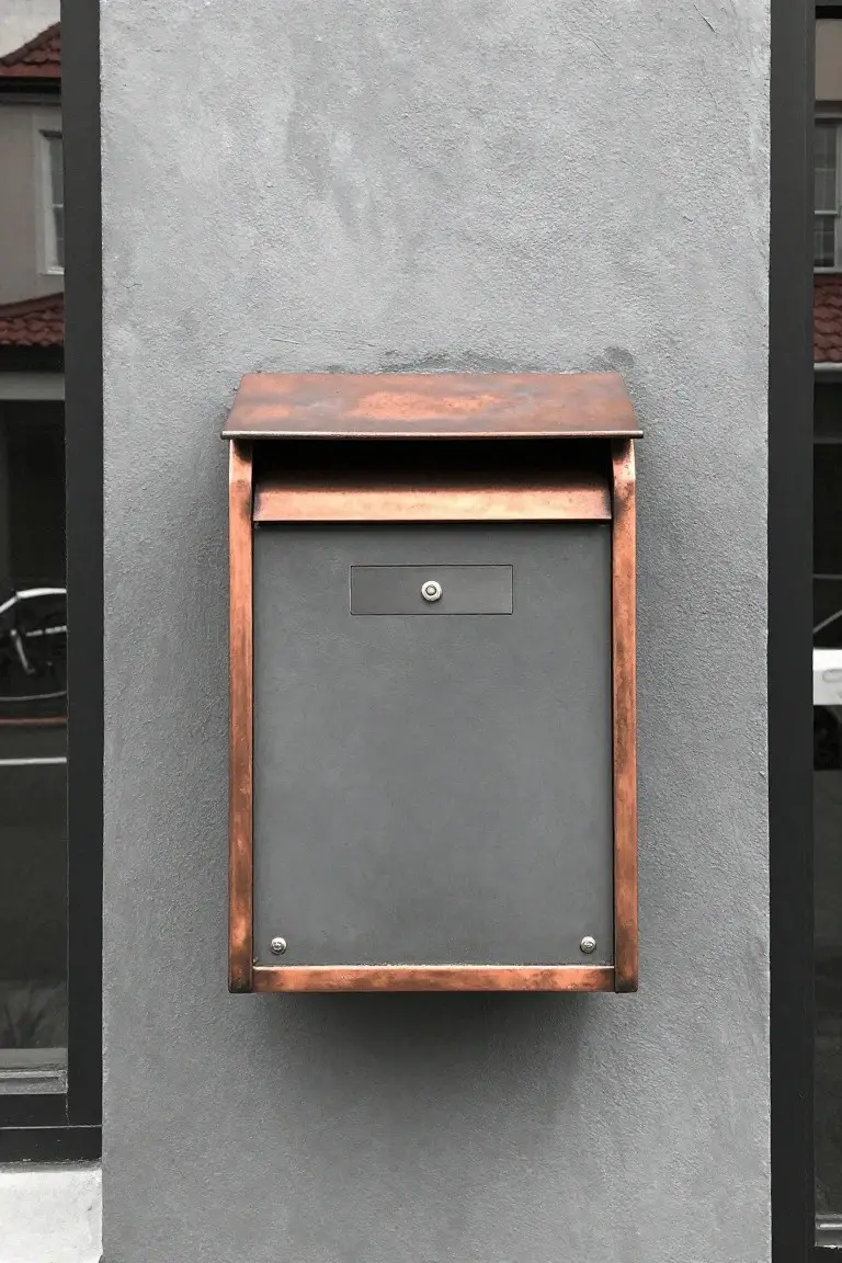 Modern neutral gray stucco wall with mounted copper mailbox and subtle hardware