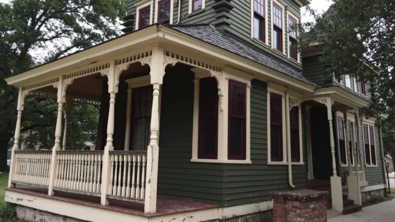 Victorian house painted in deep green siding with cream trim and red window accents under tree shade