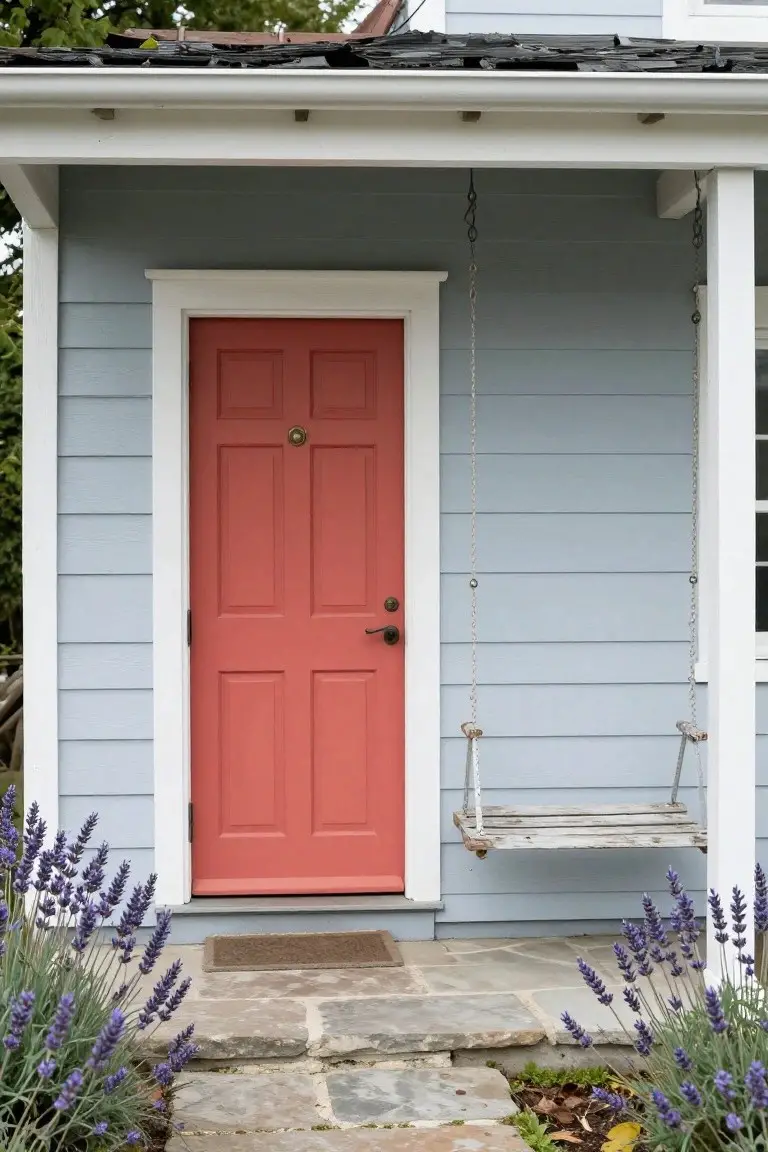 Light blue-gray clapboard house siding with red front door, white trim, porch swing, and lavender plants