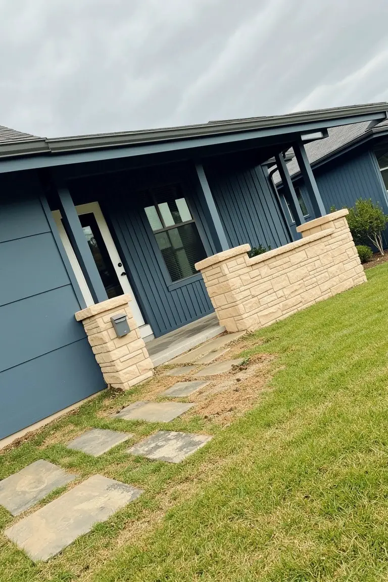 Modern home exterior with deep navy blue siding, beige stone accents, and stone pathway steps
