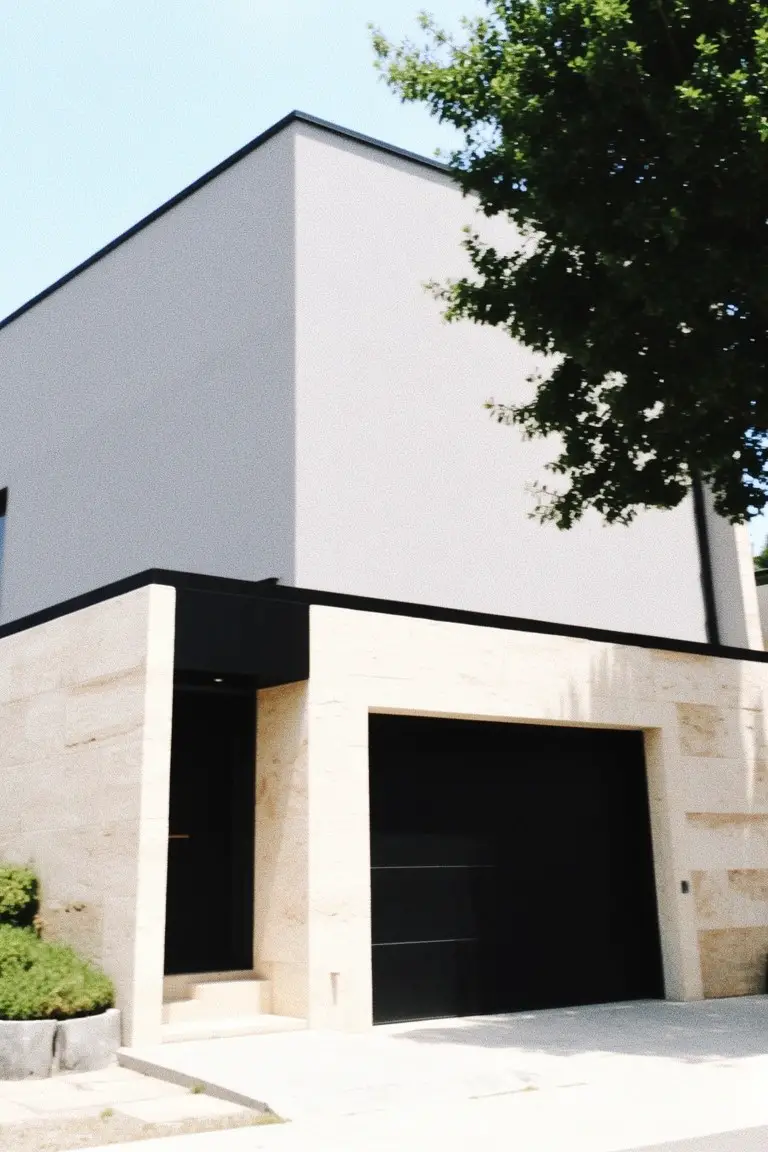 Modern minimalist house with light cool gray painted walls, black doors and garage, and beige stone foundation under a tree
