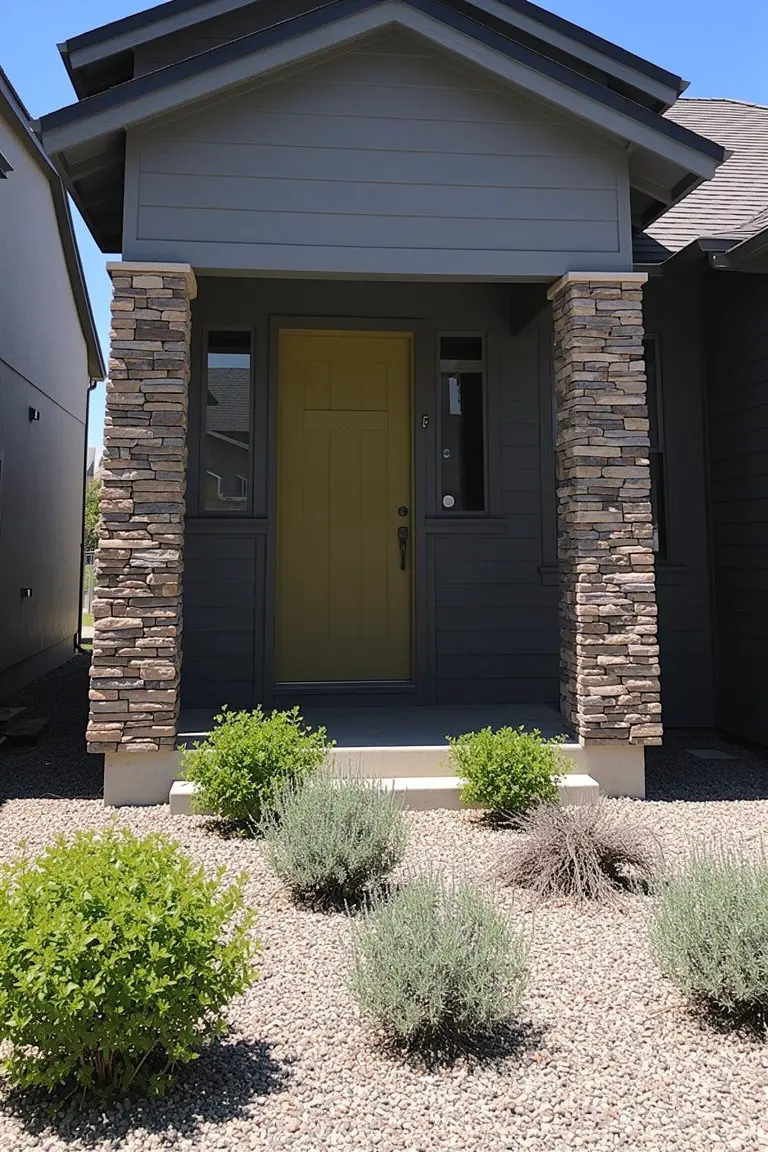 Ranch-style house with cool charcoal gray siding, stone pillars, yellow door, and desert landscaping