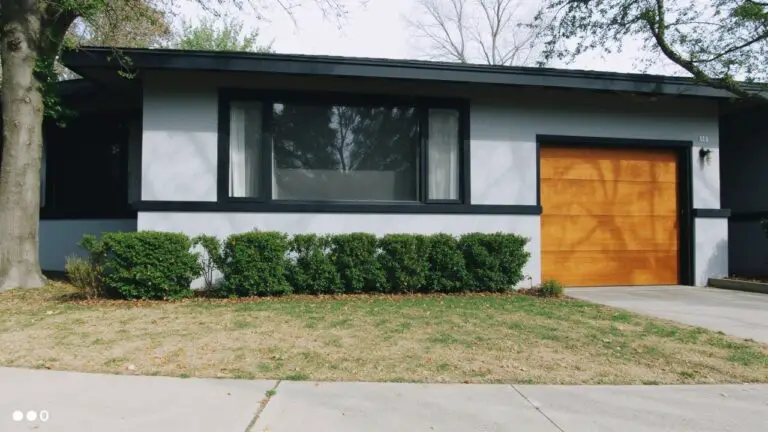Ranch house with soft blue-gray siding, orange garage door, white-trimmed windows, and landscaped front yard