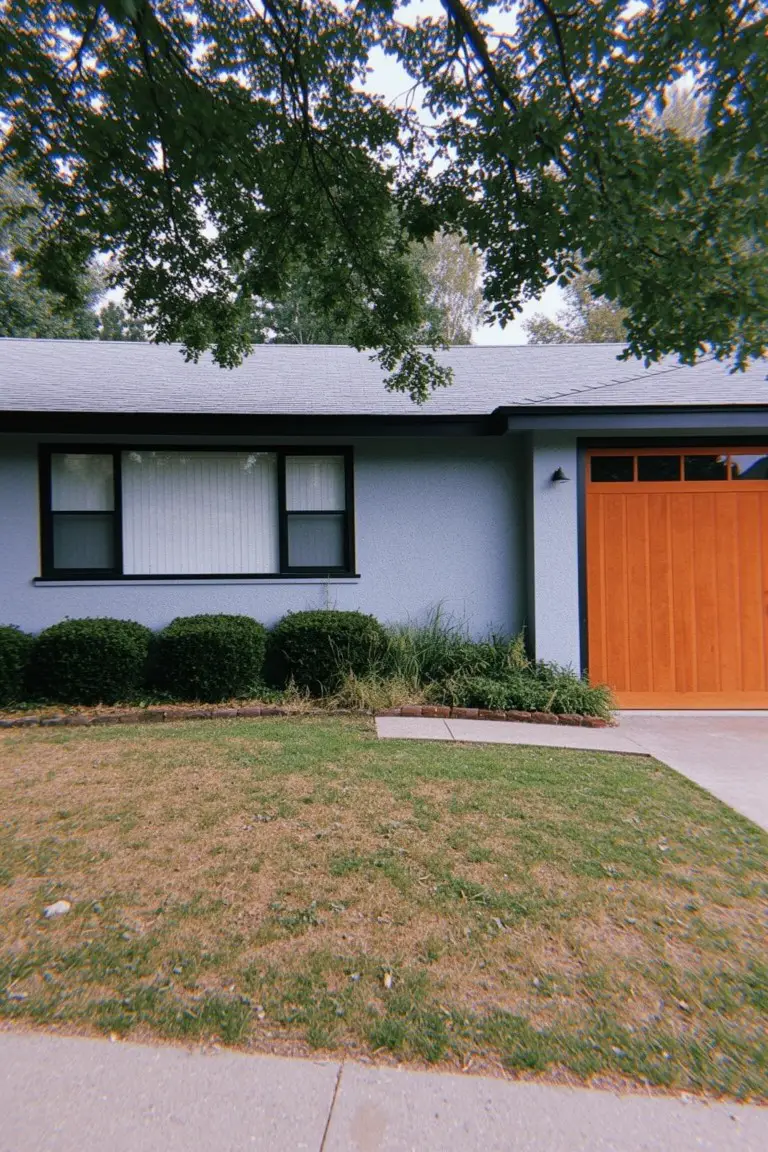 Ranch house with soft blue-gray siding, orange garage door, white-trimmed windows, and landscaped front yard