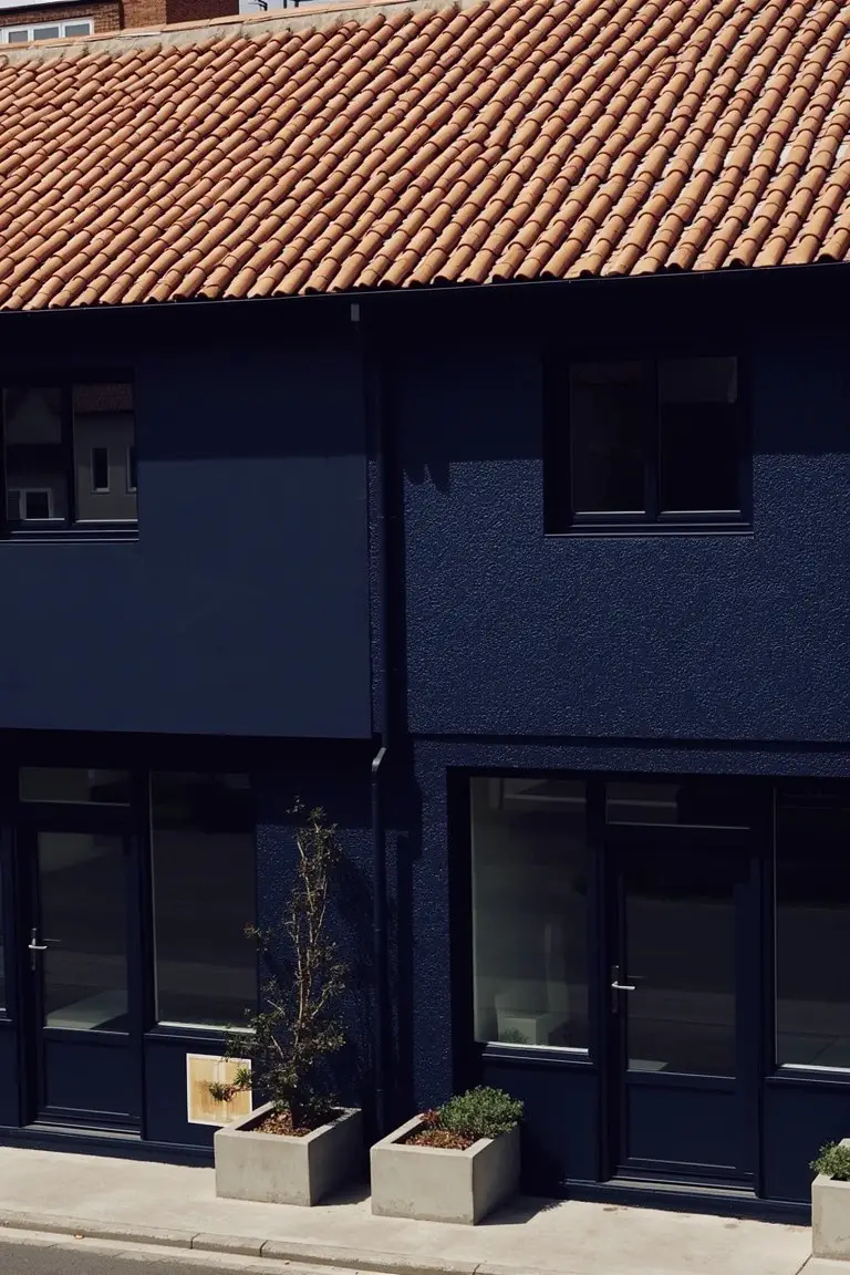 Modern two-story home exterior painted deep navy blue with large glass doors and windows, terracotta tile roof, and potted plants along the base