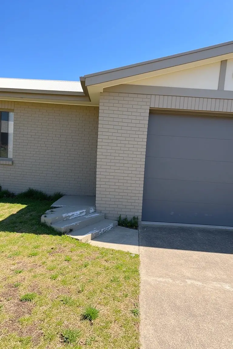 Beige brick house exterior featuring a medium gray garage door, white window trim, and concrete steps