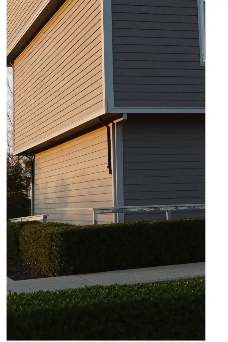 House exterior with warm greige clapboard siding, white trim, and neat hedge border