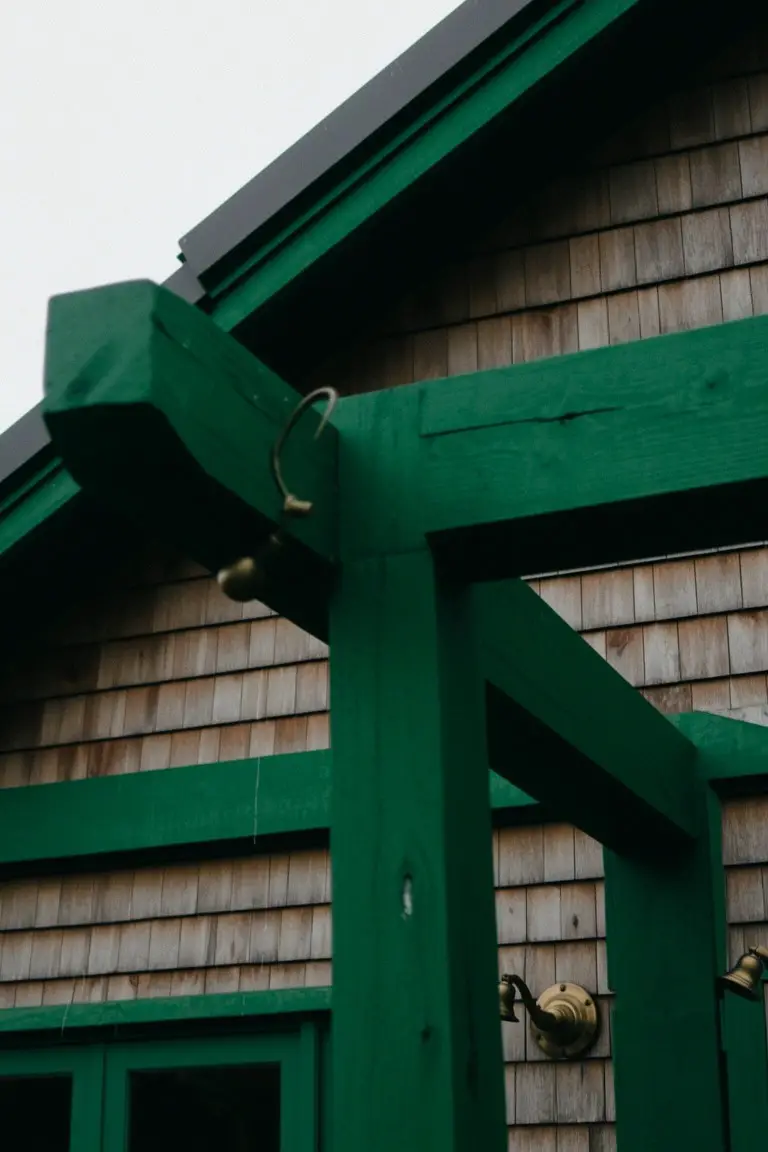Deep green painted beams and trim framing a door on shingle house exterior