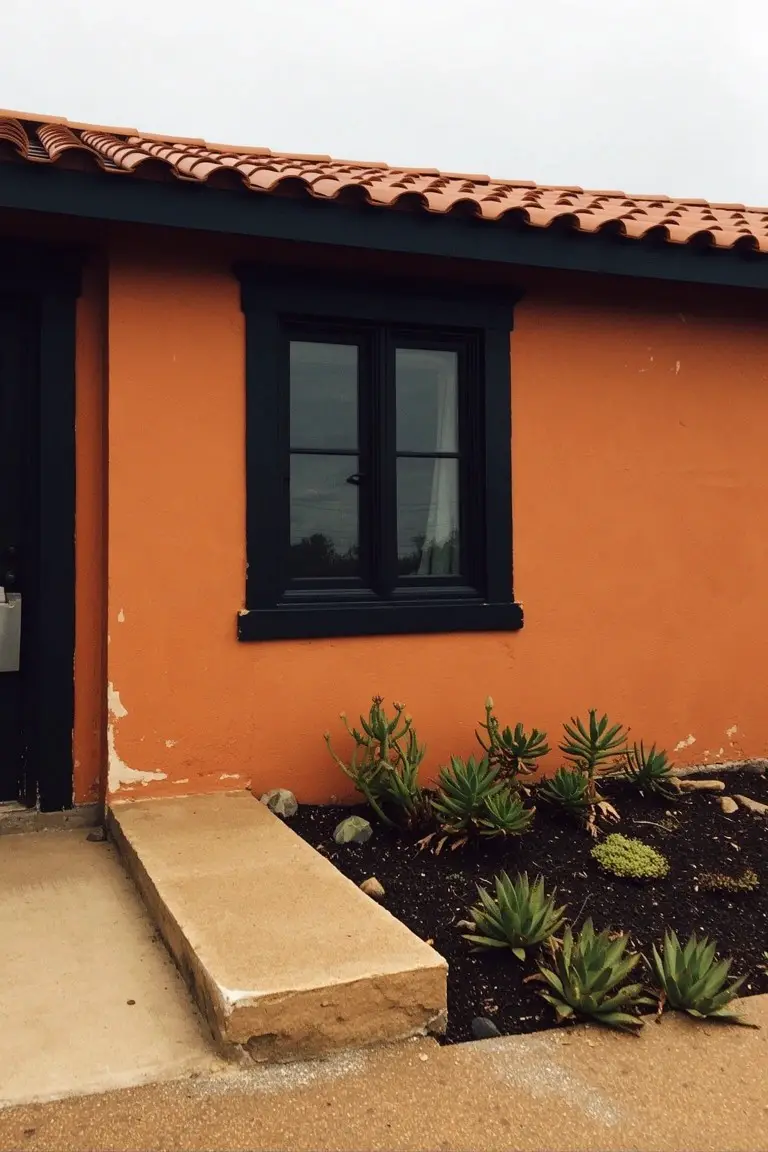 Warm terracotta orange stucco house exterior with black window and door frames, red tile roof, and succulents in front