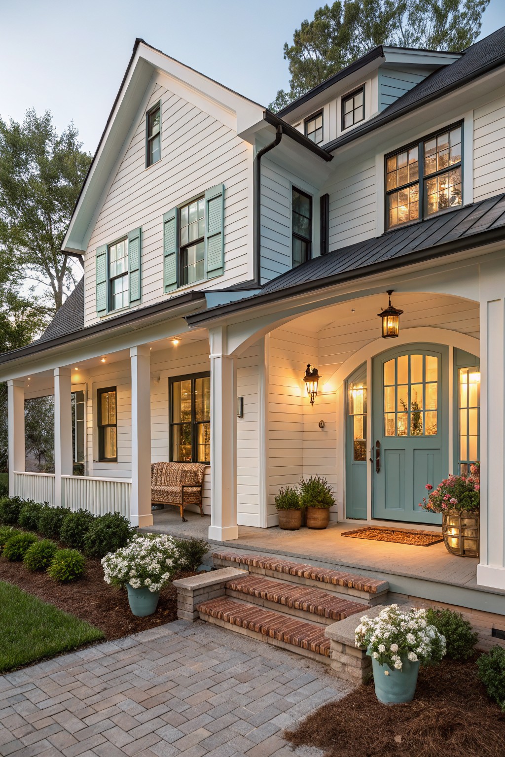White clapboard house exterior with teal arched front door, covered porch supported by columns, lanterns, brick steps, potted plants, and brick pathway.