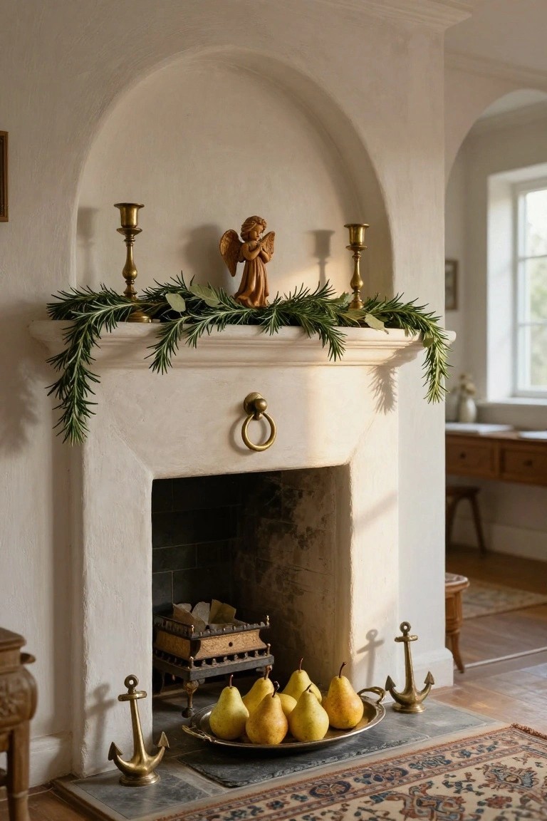 White stucco fireplace mantel decorated with brass candlesticks, rosemary and eucalyptus garland, wooden angel figurine, and a silver dish of yellow pears on the hearth flanked by brass anchors.