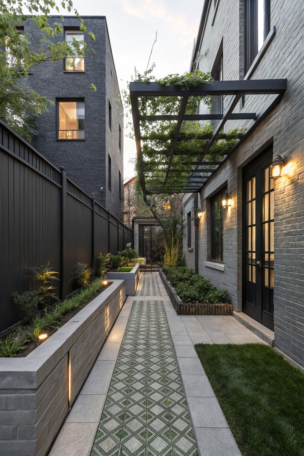 Narrow side yard pathway with green diamond-patterned tiles between gray brick walls, concrete planters filled with plants, wall-mounted lights, and a vine-covered metal pergola overhead.