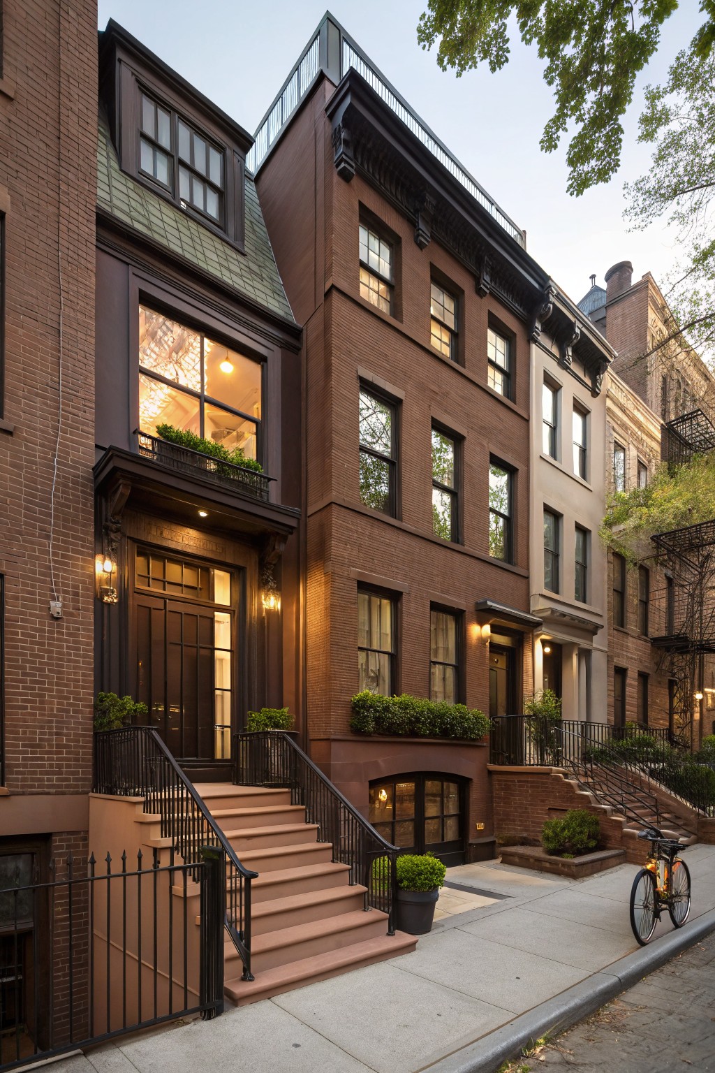 Brown brick rowhouse exterior featuring a sloped green metal roof, large glass window with plants, black front door, entry steps with railing, and adjacent townhouses on a sidewalk with a bicycle parked nearby.