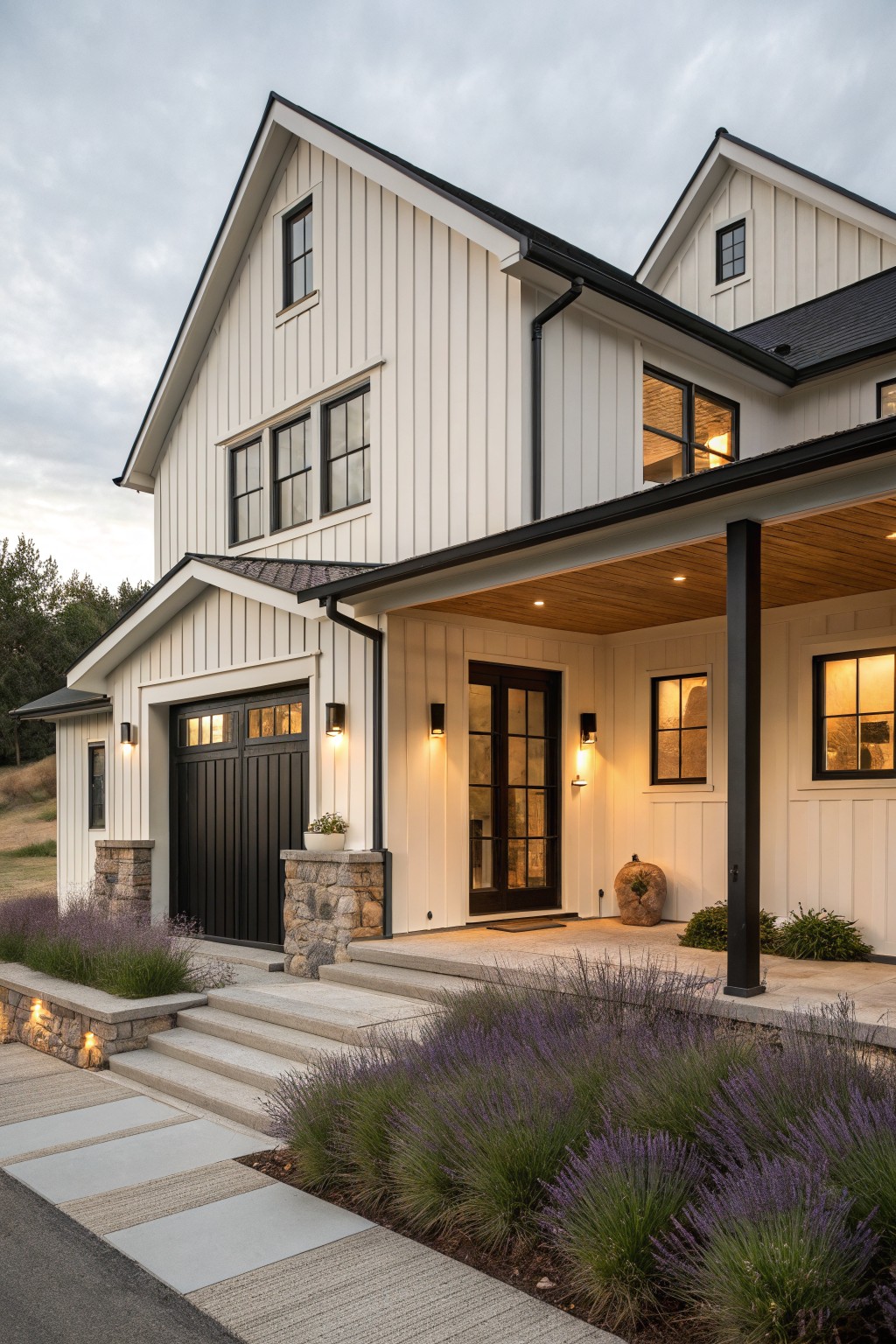 A two-story white board-and-batten house with black-trimmed windows, dark garage door, covered entry porch, stone accents, and purple lavender plants along the front path and steps.