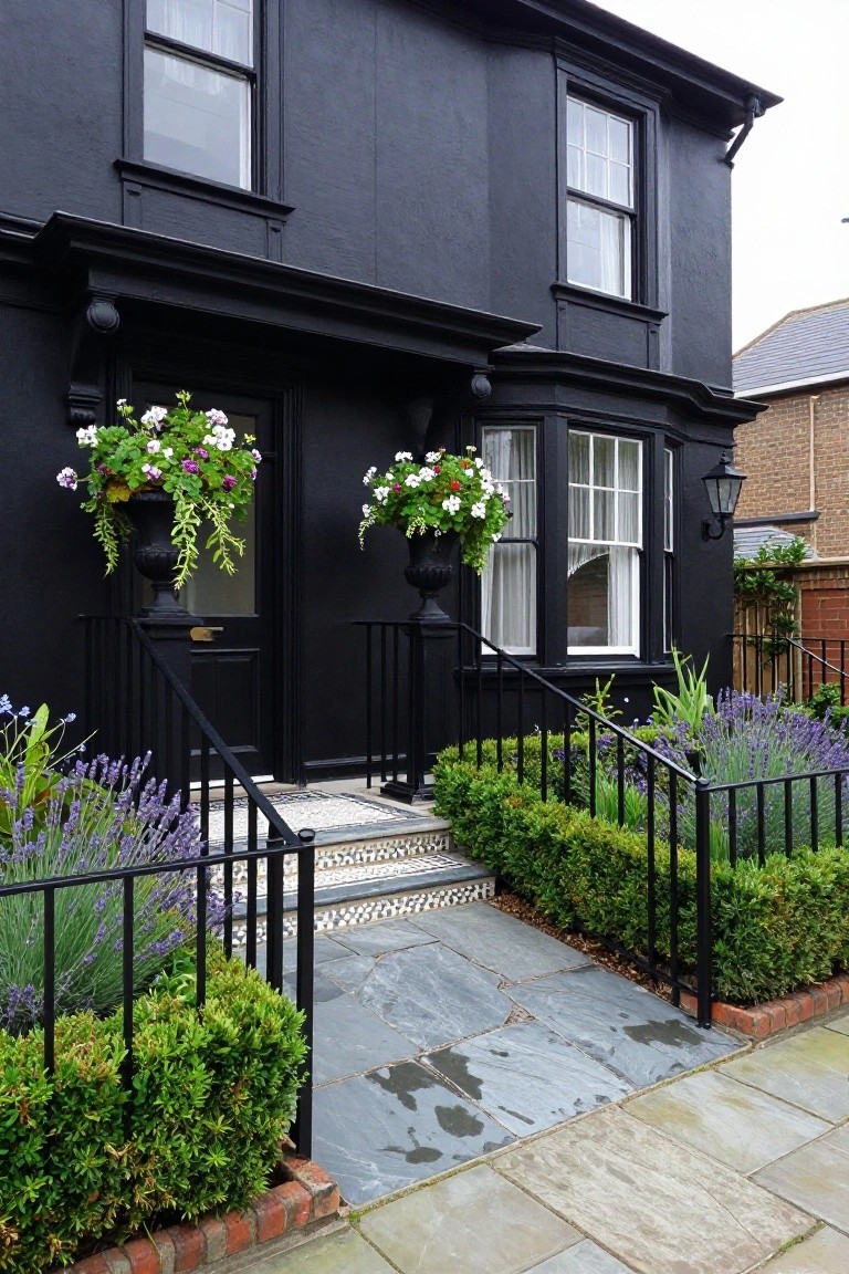 Black painted Victorian-style house exterior with front steps, black railings, lavender flower beds, boxwood hedges along a stone path, and white flower baskets flanking the doors.