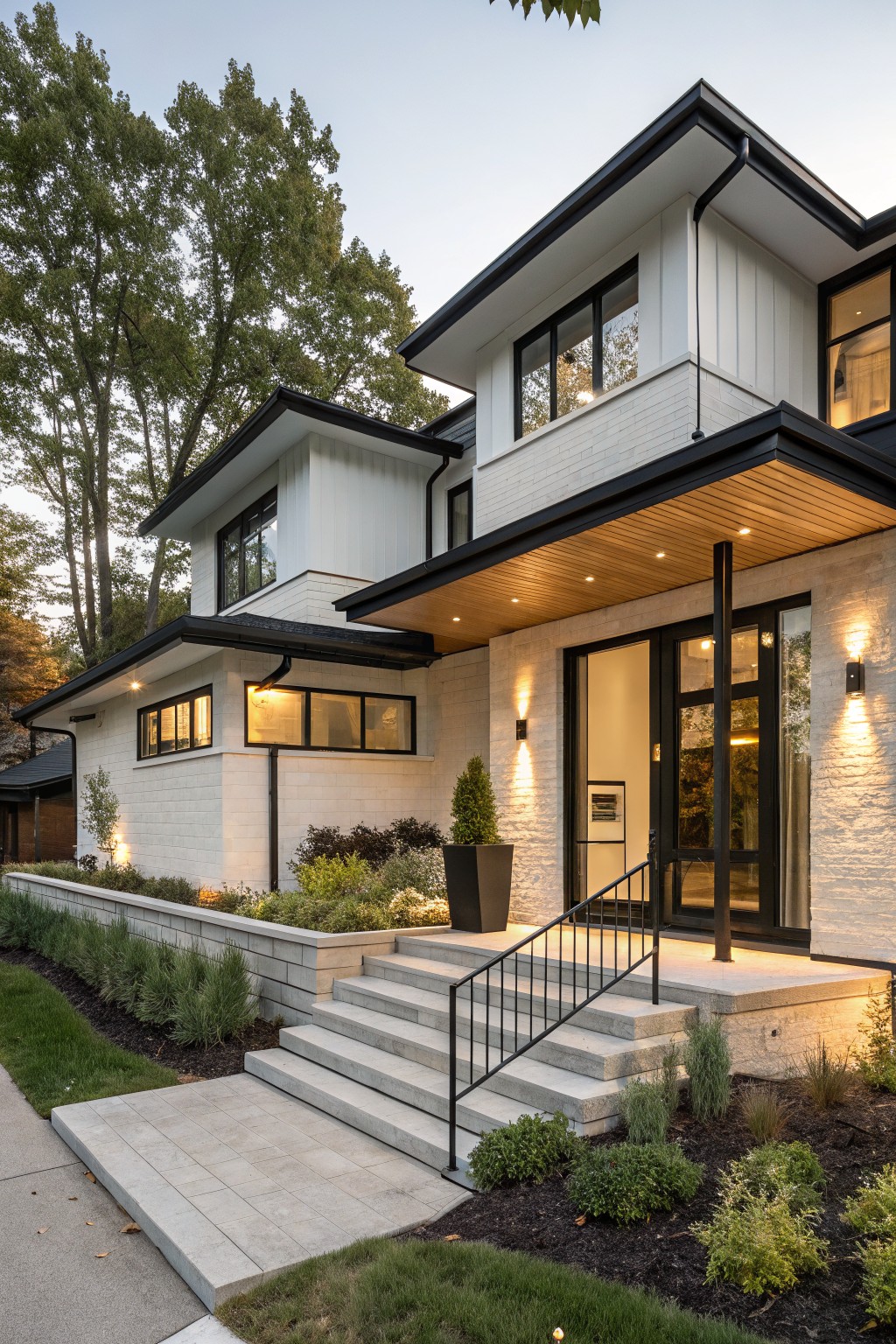 Modern two-story house exterior with white brick base and siding, black trim on windows, door, and rooflines, cantilevered entry porch with wood ceiling and black posts, concrete steps, and low shrubs in front.