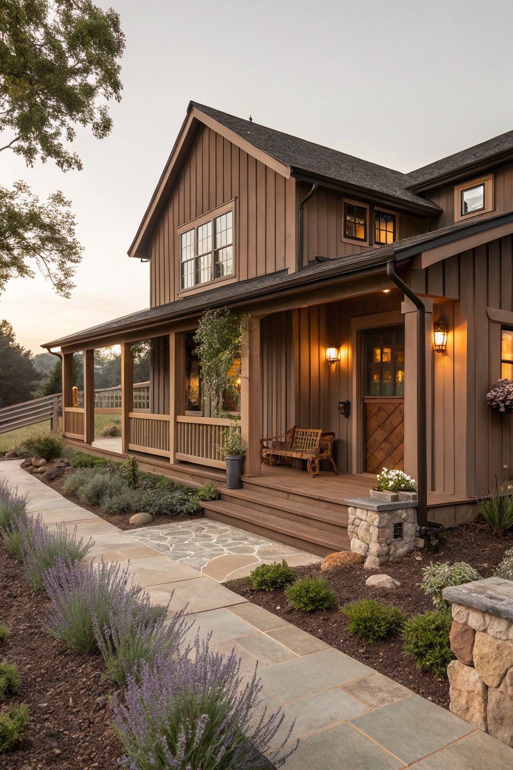 Brown board-and-batten sided ranch house exterior with covered porch, wooden bench on steps, wall lanterns, potted plants, stone pathway lined with lavender and shrubs leading to entry door at dusk.