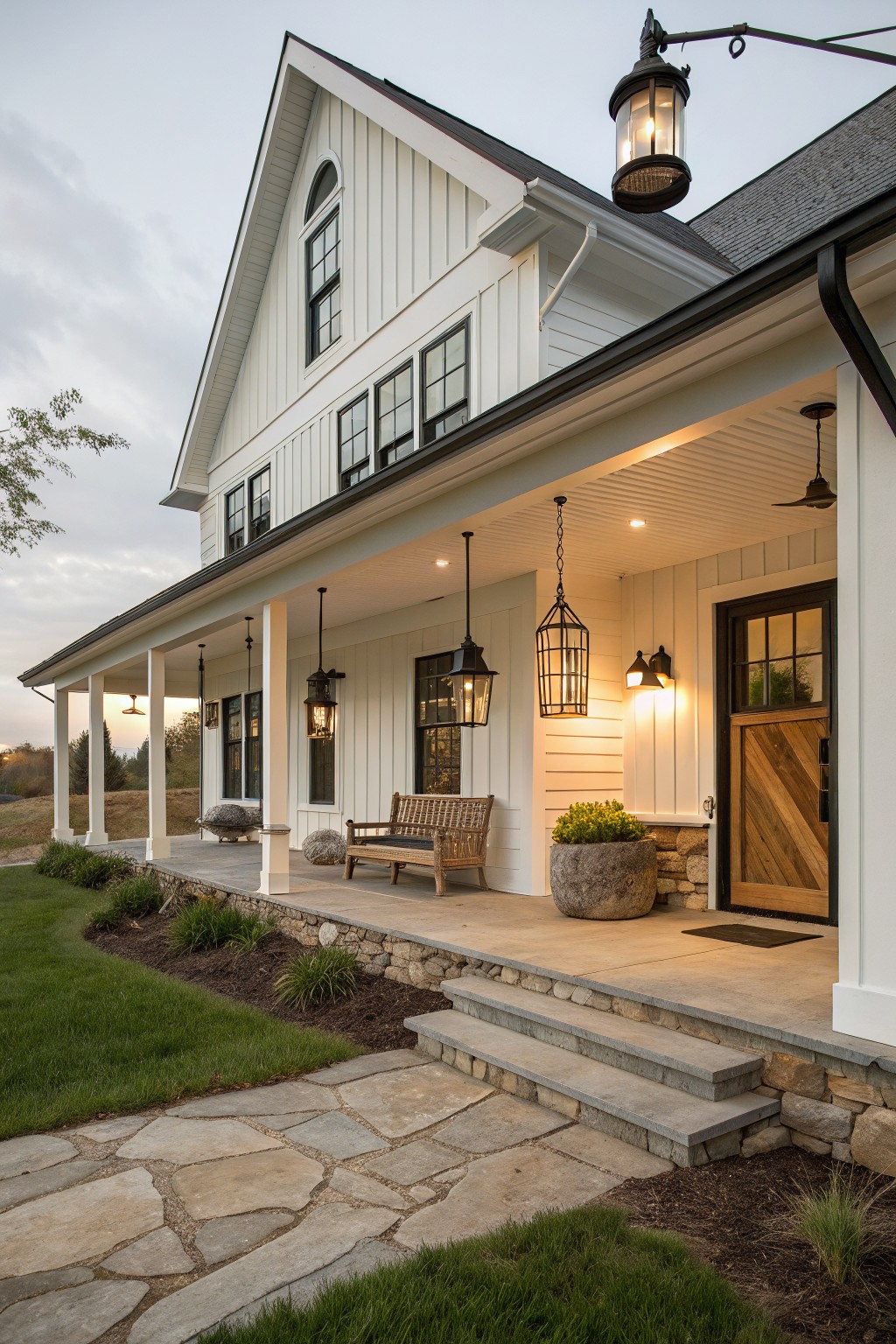 White shiplap farmhouse house exterior with wraparound porch, hanging black lantern lights, wooden bench, potted plants, and flagstone path leading to dark wood entry door.