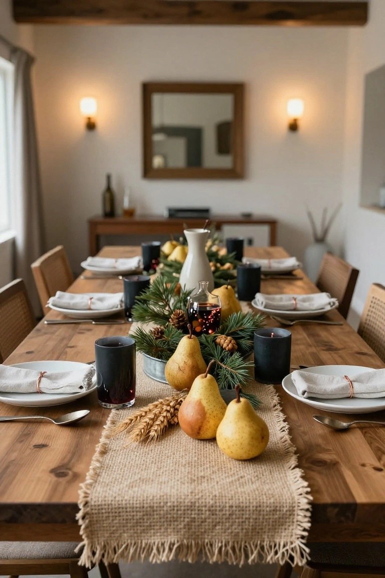 Wooden dining table in a light room with burlap runner centered and topped with yellow pears, wheat, pine branches, pinecones, and black candles, flanked by white plates, napkins with copper ties, black glasses, and additional greenery and a white pitcher.