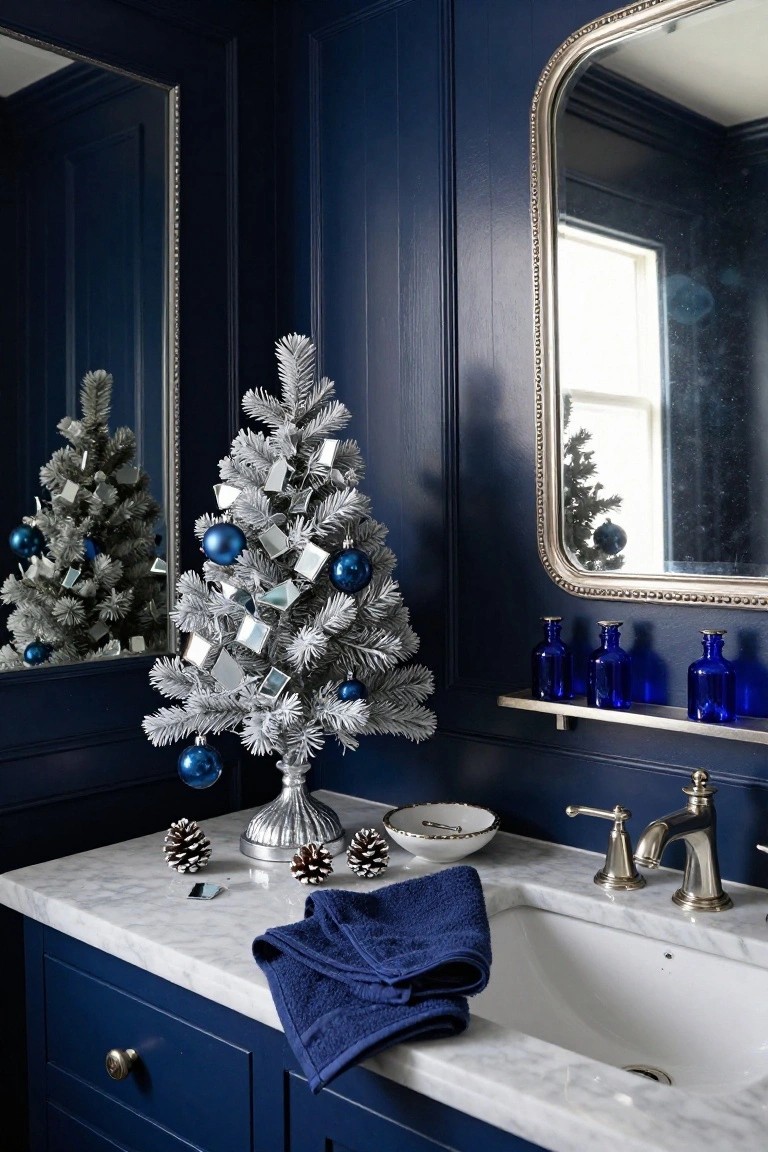 Small silver flocked artificial Christmas tree with blue and silver ornaments on a marble bathroom vanity next to the sink in a navy paneled powder room, blue towel draped over the edge and blue glass bottles on a shelf.