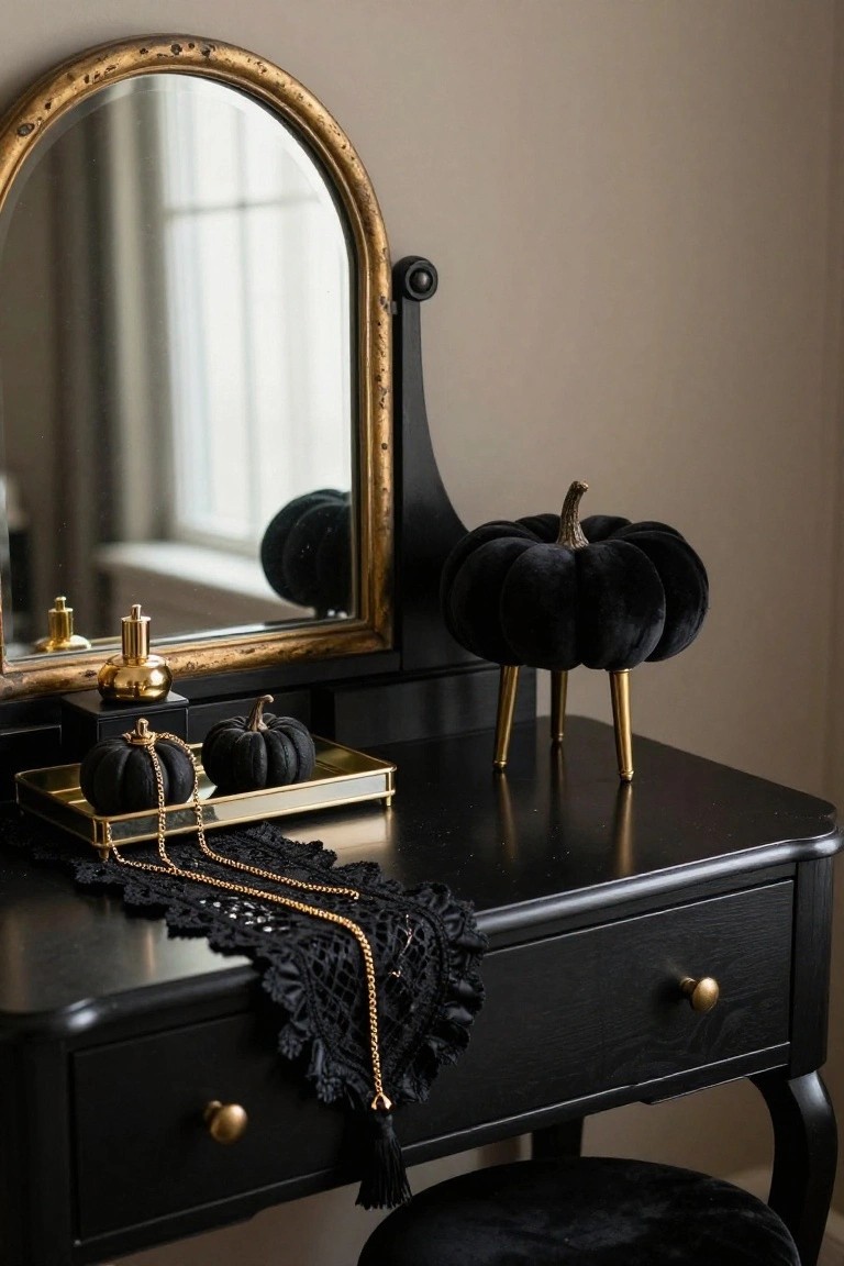 Black wooden vanity table topped with gold oval mirror, gold perfume bottles, small black velvet pumpkins on gold tray with black lace runner and gold chain necklace, gold-accented black pumpkin on legged stand nearby, black velvet stool in front.