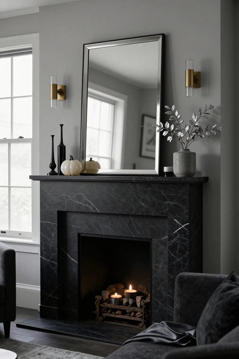 White marble fireplace mantel decorated with black candlestick holders holding black taper candles, small white pumpkins, glass cylinder candles, and a gold-framed mirror above, with velvet armchairs and a bowl of figs on the hearth.