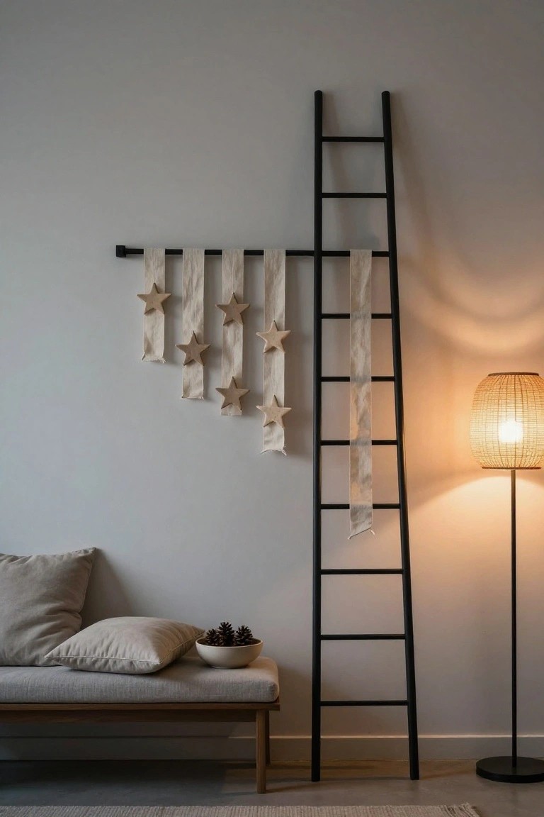 Black ladder leaning against light gray wall with beige linen banners hanging from a rod at the top, each adorned with wooden stars, next to low beige bench sofa, pillows, pinecone bowl, and rattan floor lamp on wood floor.