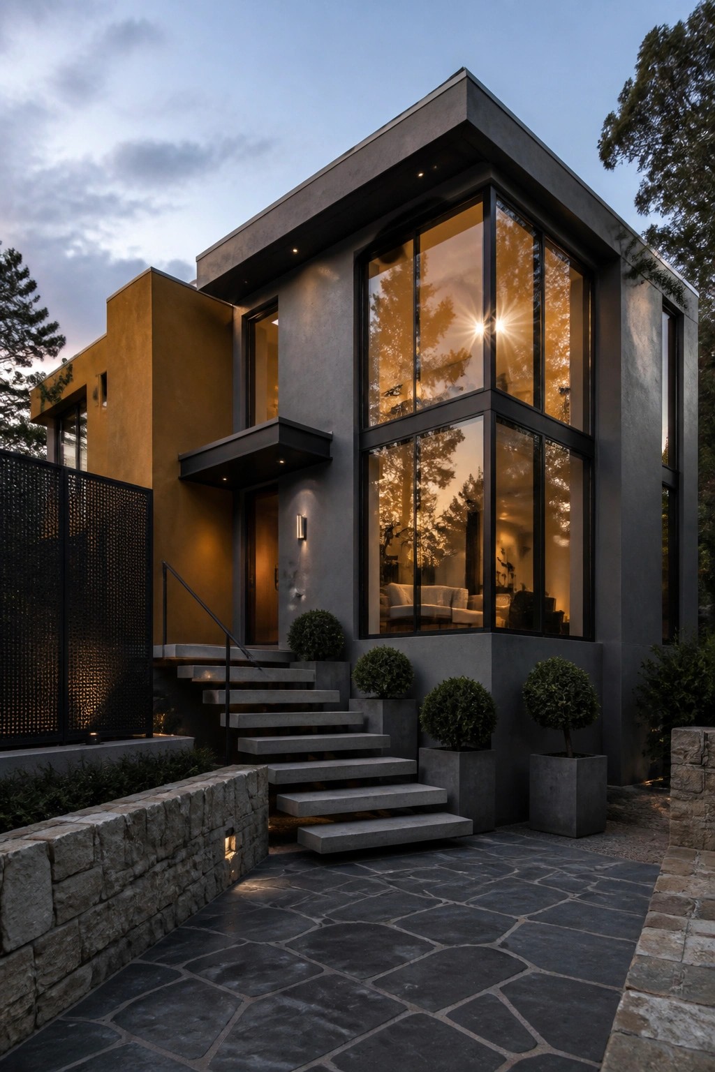 Modern concrete house with large glowing windows, stone steps, and potted plants at dusk.