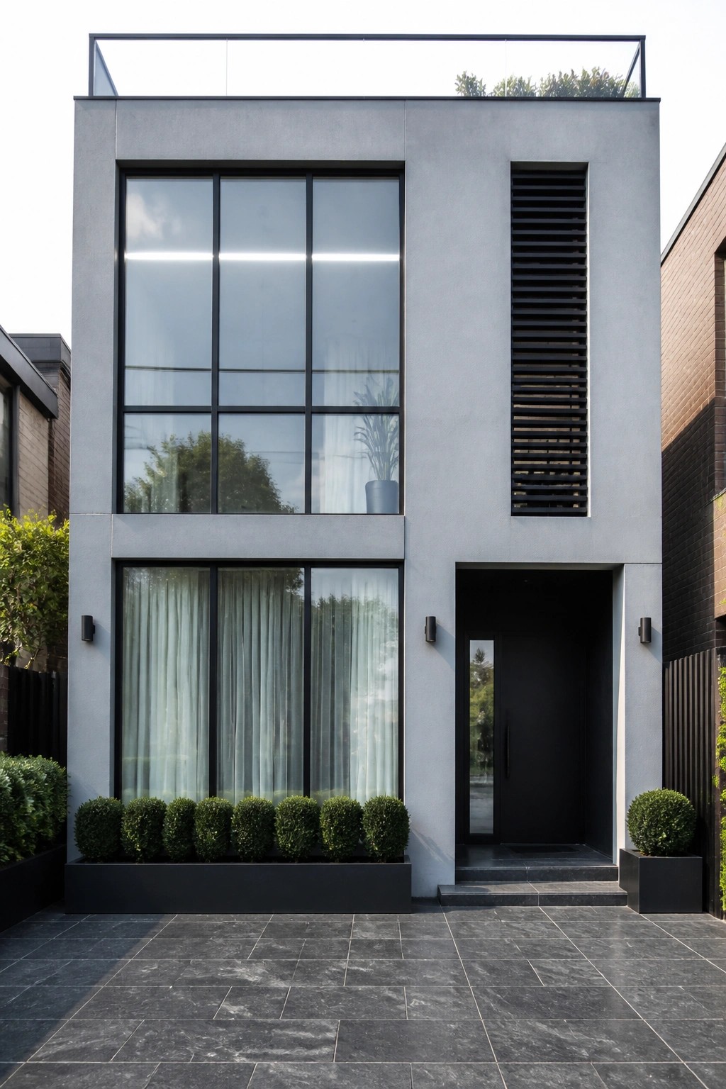 A modern two-story house with light gray exterior walls, large black-framed windows, and a black front door set on a paved driveway.