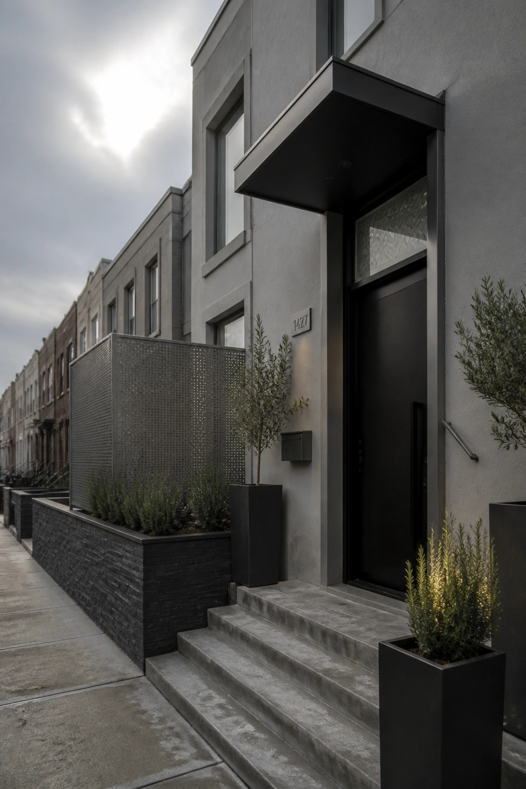 Modern gray townhouse with black door, concrete steps, and potted plants.