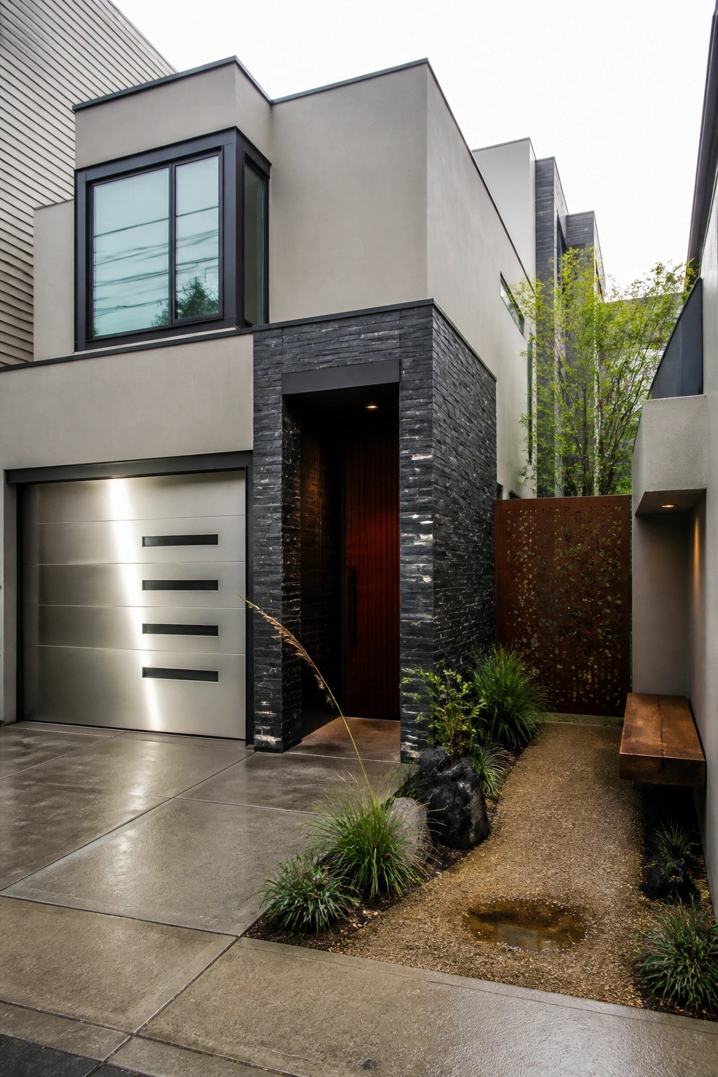 Modern house exterior with light gray walls, dark stacked stone around the entry, a metallic garage door, and a wood front door.