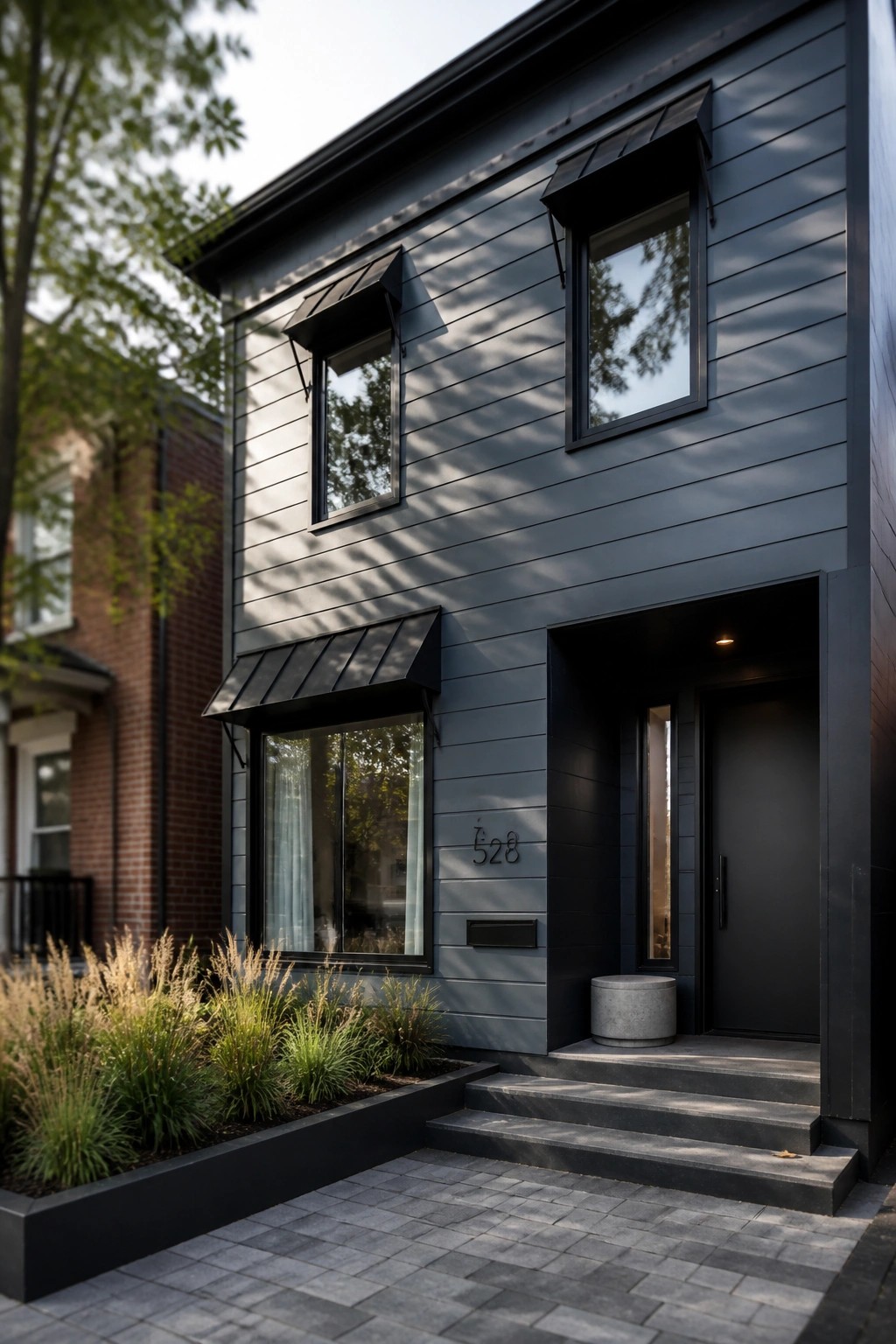 Modern two-story house with dark gray horizontal siding, black-framed windows, black door, and concrete steps leading to the entrance.