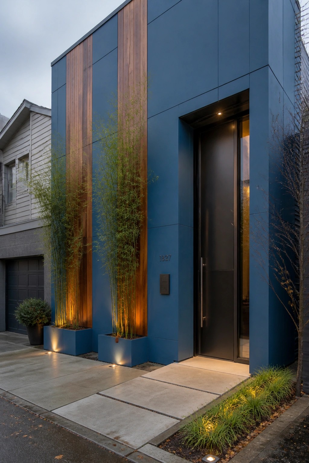 A modern house facade painted deep blue with vertical wood paneling, a black front door, and tall bamboo plants in square blue planters beside the entrance.