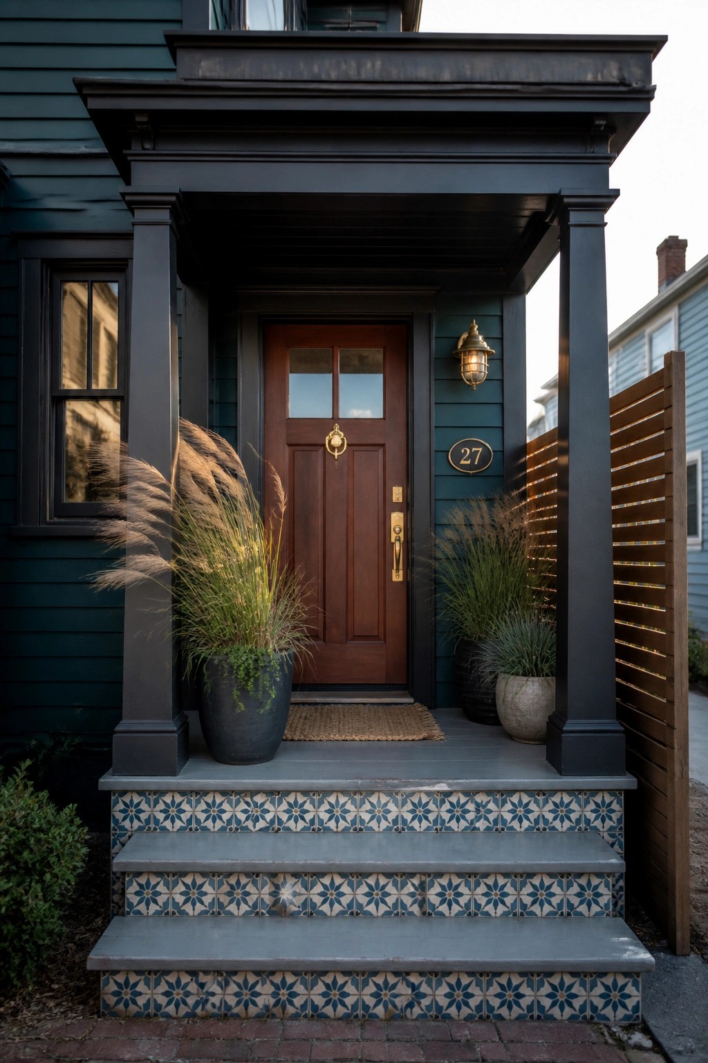 Dark teal house porch with wooden door, potted grasses, and tiled steps