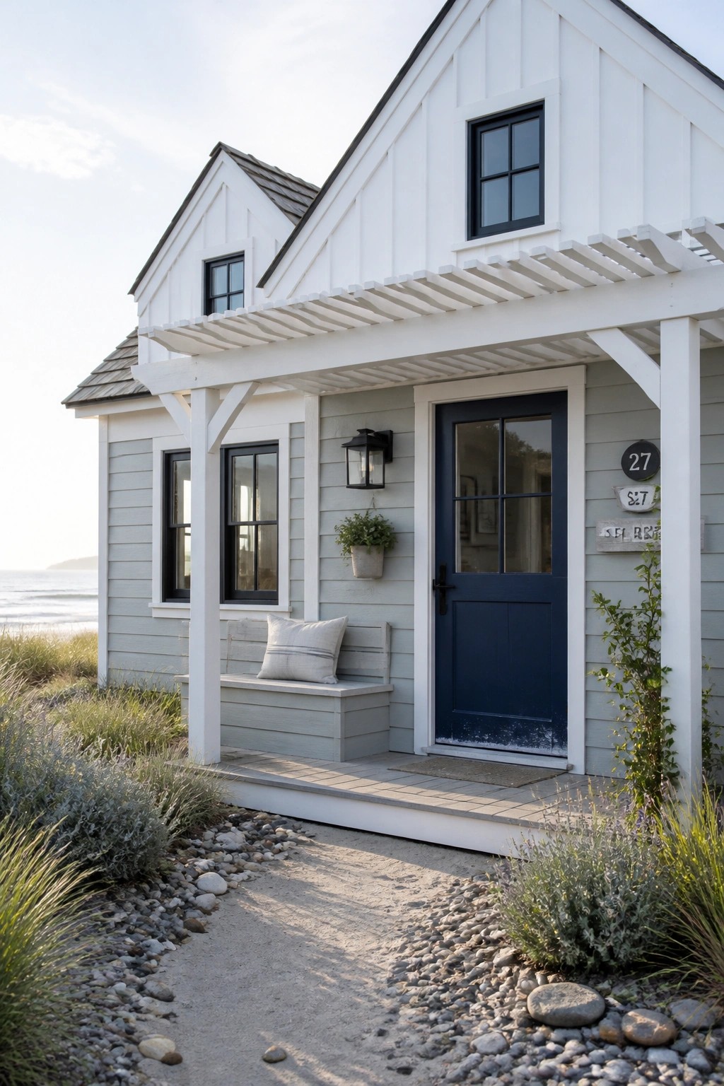 White beach cottage with navy door, porch bench, and ocean view