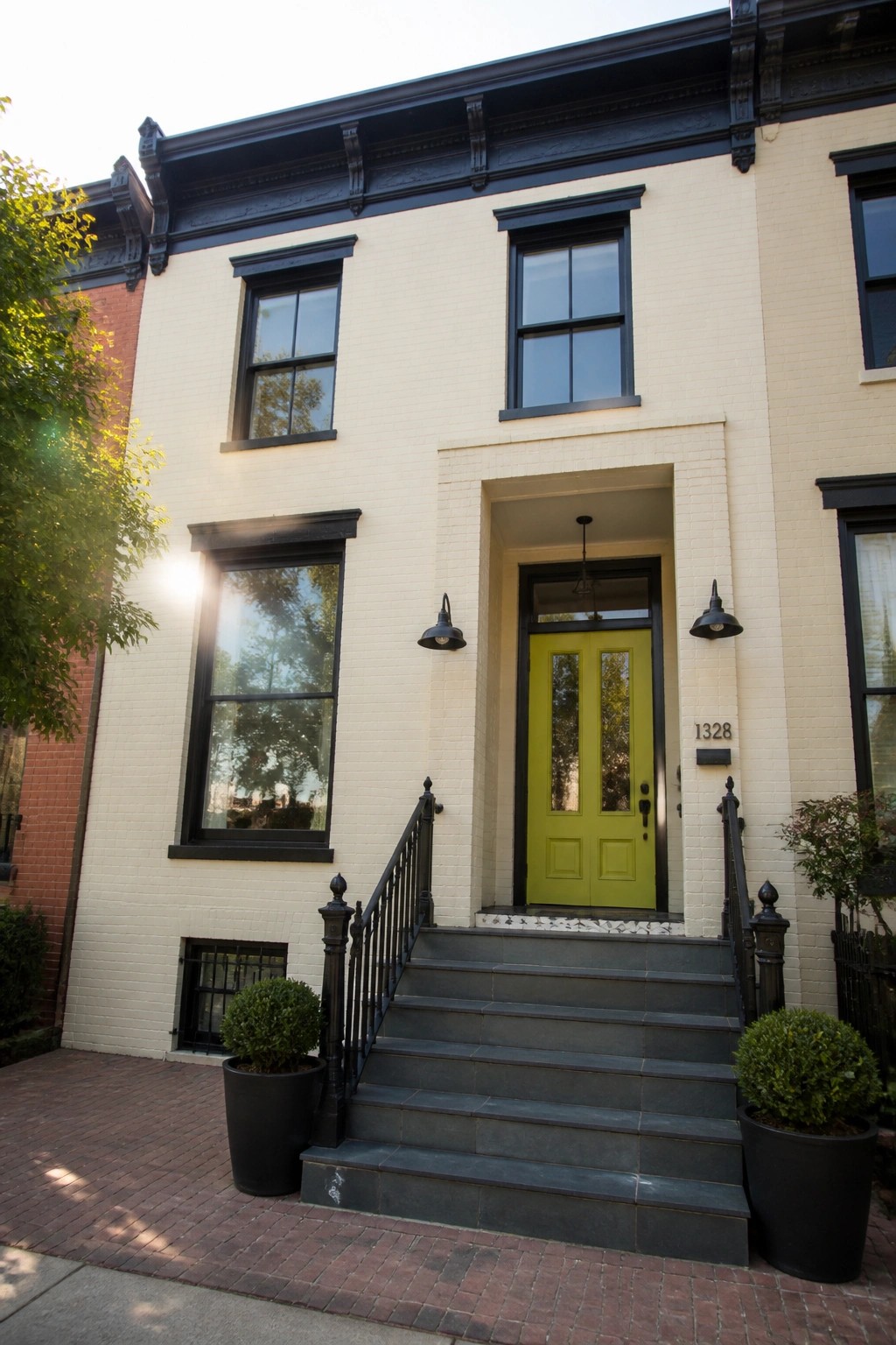 A white painted brick row house with black window trim, a lime green front door, and dark stone steps leading to the entrance.
