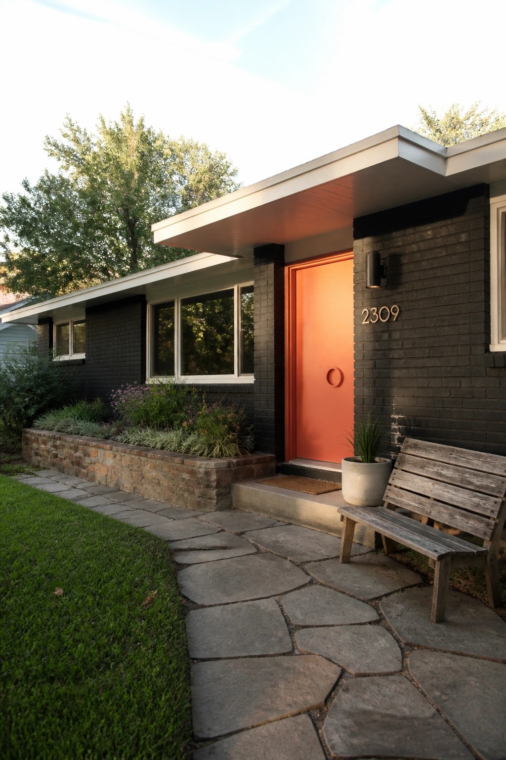 Front view of a single-story house with dark painted brick, a bright orange front door, white trim, and a stone pathway leading to the entrance.