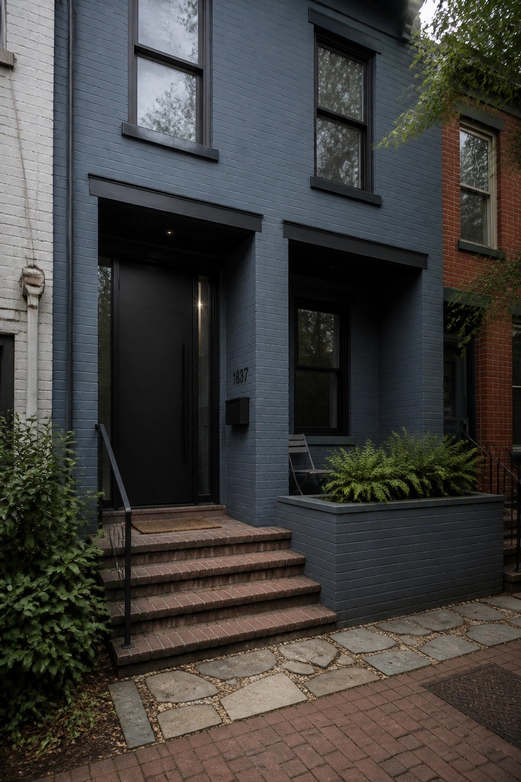 Dark blue brick townhouse with black door, steps, and fern-filled planter.